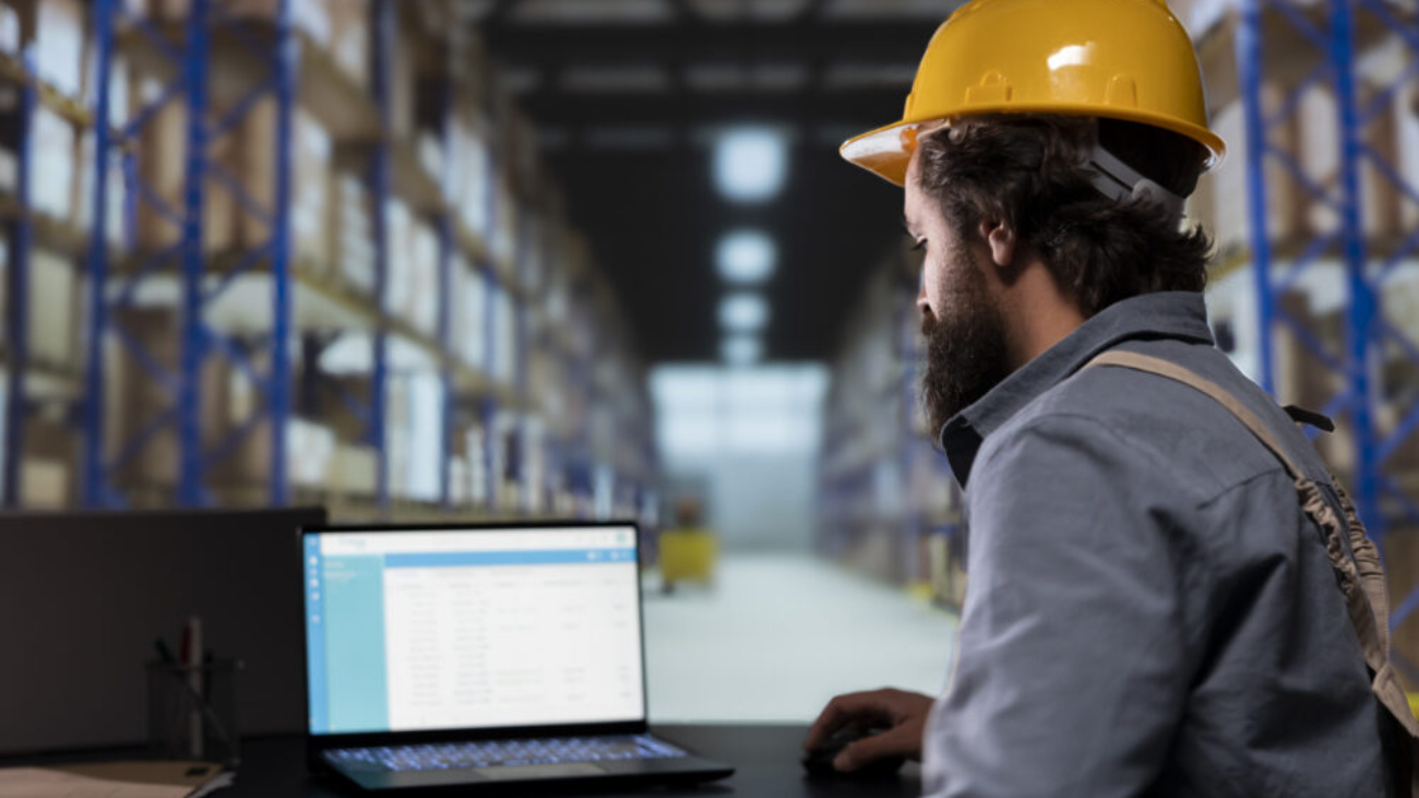 Worker using a laptop in a distribution warehouse, illustrating how a Sage warehouse management system supports inventory tracking and operational efficiency.
