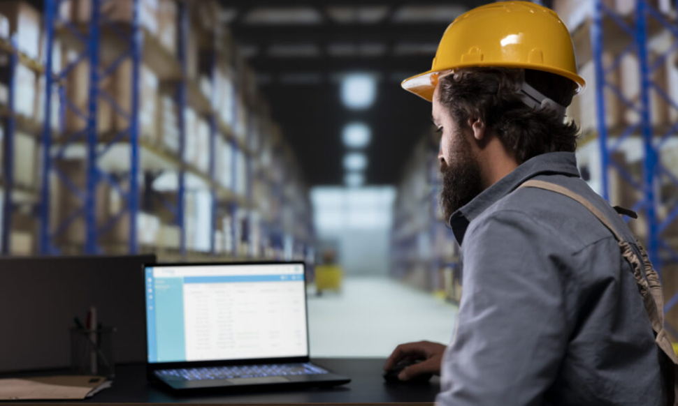 Worker using a laptop in a distribution warehouse, illustrating how a Sage warehouse management system supports inventory tracking and operational efficiency.