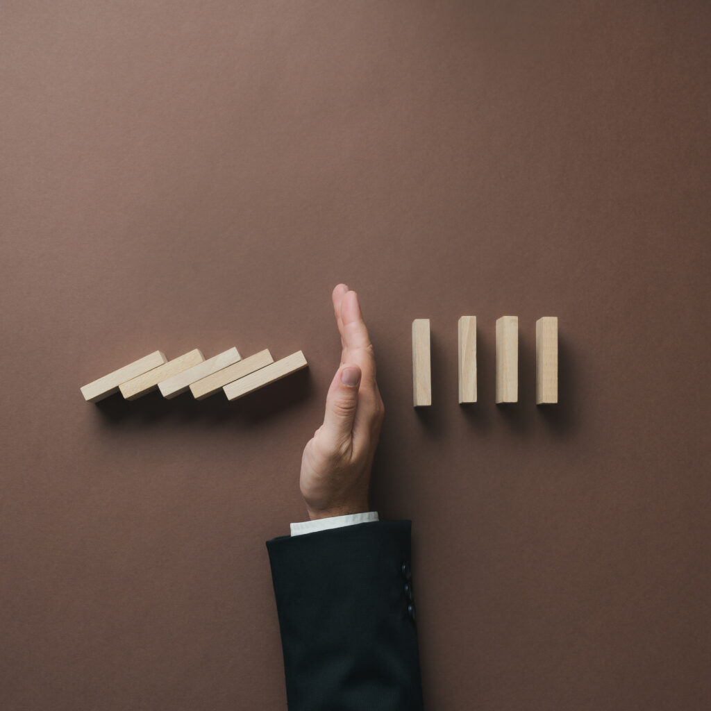 A hand stopping a row of falling wooden dominoes, symbolising control and preventing disruption, representing how upgrading from Sage 50 to Sage 200 or Sage Intacct can help businesses scale efficiently.
