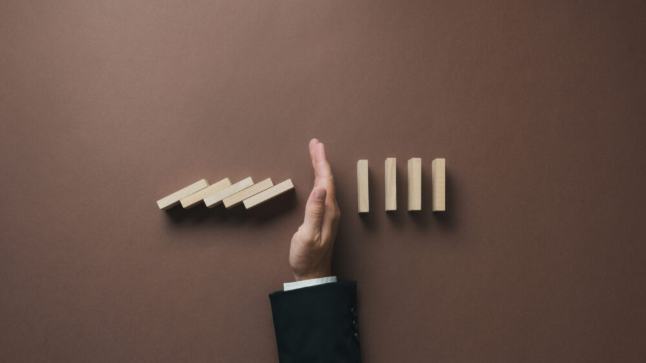 A hand stopping a row of falling wooden dominoes, symbolising control and preventing disruption, representing how upgrading from Sage 50 to Sage 200 or Sage Intacct can help businesses scale efficiently.
