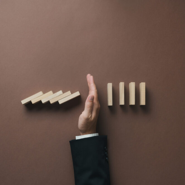 A hand stopping a row of falling wooden dominoes, symbolising control and preventing disruption, representing how upgrading from Sage 50 to Sage 200 or Sage Intacct can help businesses scale efficiently.