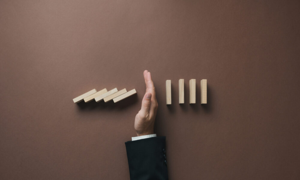 A hand stopping a row of falling wooden dominoes, symbolising control and preventing disruption, representing how upgrading from Sage 50 to Sage 200 or Sage Intacct can help businesses scale efficiently.