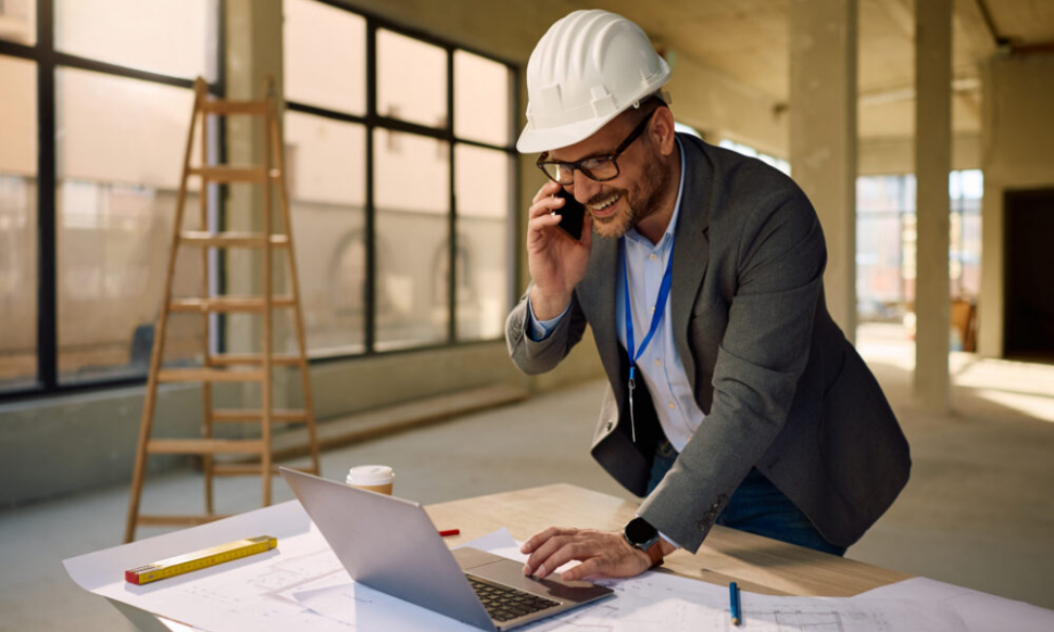 Construction engineer reviewing project finances using Sage for Construction software on a laptop while speaking on the phone.