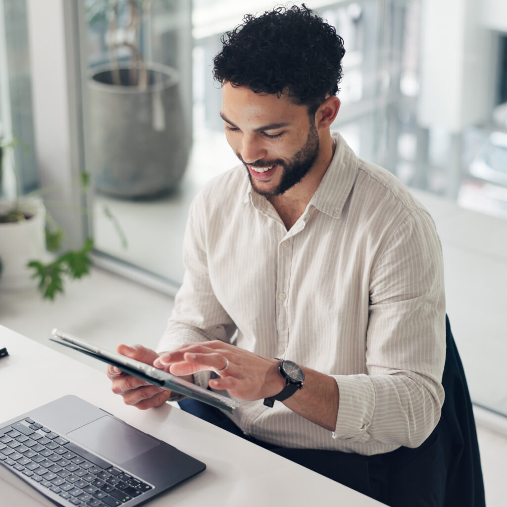 Happy businessman using a tablet and laptop in the office, managing projects with Sage Intacct professional services software.