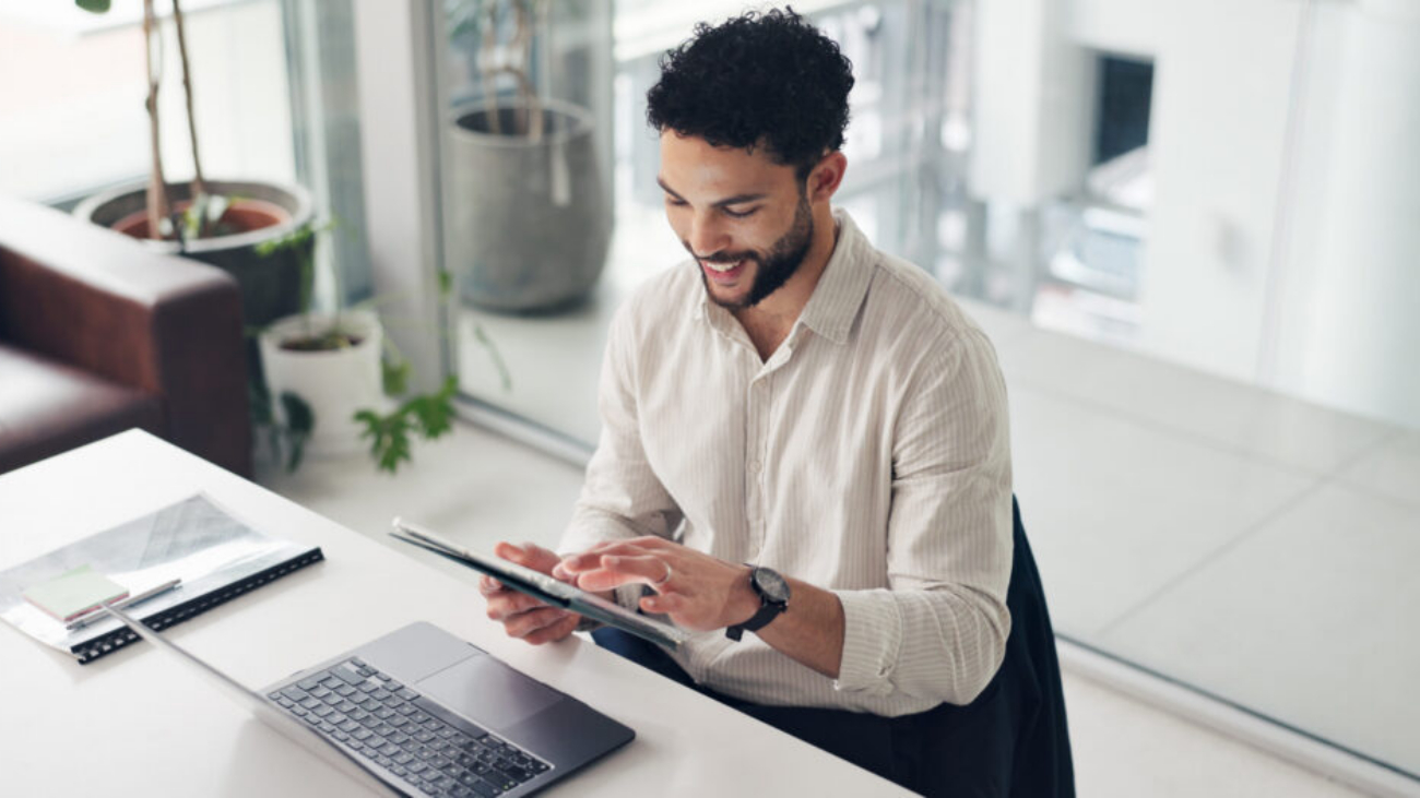 Happy businessman using a tablet and laptop in the office, managing projects with Sage Intacct professional services software.