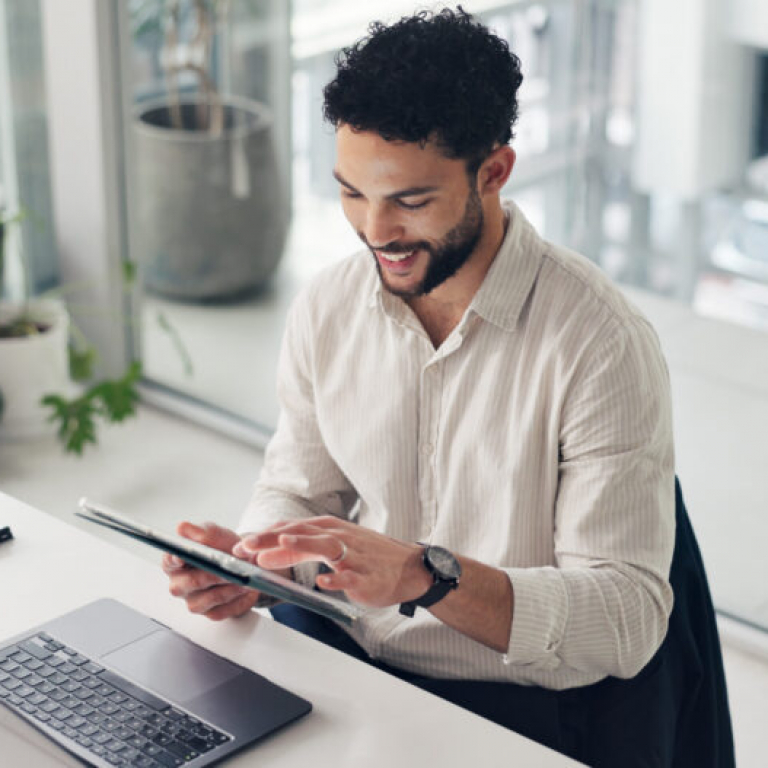 Happy businessman using a tablet and laptop in the office, managing projects with Sage Intacct professional services software.