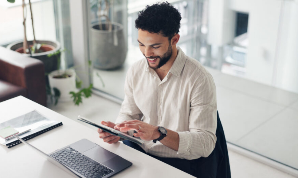 Happy businessman using a tablet and laptop in the office, managing projects with Sage Intacct professional services software.